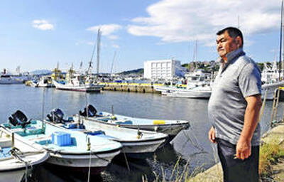 漁船が浮かぶ小名浜の海を見つめる馬目さん。「原発事故処理の責任の片棒を担ぐつもりはない」と言い切る＝いわき市