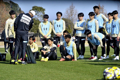 田村監督（手前）から練習メニューの説明を受ける選手＝２５日、鹿児島県立サッカー・ラグビー場