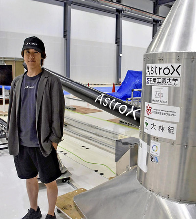 ロケットと気球の間に置く姿勢制御装置を前に「宇宙開発でジャパン・アズ・ナンバーワンを目指す」と語る小田代表。奥はロケット