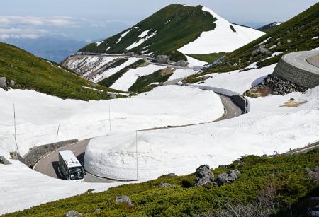 　冬季閉鎖期間が終わり開通した「乗鞍スカイライン」で、残雪の中を走るバス＝１５日朝、岐阜県高山市