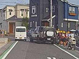 　埼玉県三郷市の市道で、小学生らの脇に止まった車（右）＝１４日（住民提供）