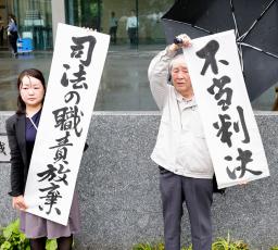 　生活保護費の基準額引き下げを巡る訴訟の控訴審判決を受け、福岡高裁前で「不当判決」などと書かれた紙を掲げる原告ら＝２１日午後