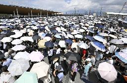 強い日差しの中、日傘を差して大阪・関西万博の入場ゲートに並ぶ大勢の人たち。万博は13日で開幕3カ月の折り返し=12日、大阪市此花区の夢洲