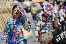 　厳しい暑さとなった大阪・関西万博の会場で、うちわで日差しを避けながら歩く人たち＝２６日午後、大阪市此花区の夢洲
