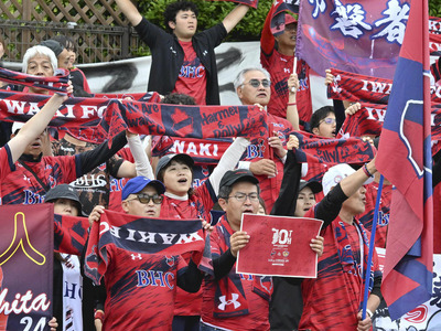 福島民友の特別号外やタオルを掲げてスタンドを真っ赤に染めたいわきサポーター。今季苦戦するチームを応援で支えている＝ハワイアンズスタジアムいわき