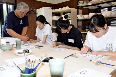 職人の根本さん（左）から絵付けの技法を学ぶ参加者