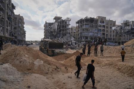 　１８日、ガザ南部ハンユニスで人質の遺体を捜索するイスラム組織ハマスの武装メンバーを見守るパレスチナ人（ＡＰ＝共同）