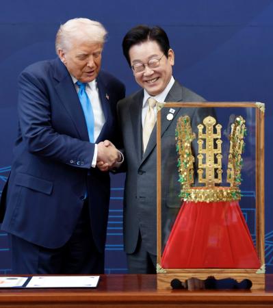 韓国・慶州で、トランプ米大統領(左)に「天馬塚金冠」のレプリカを贈呈し握手する李在明大統領=29日(聯合=共同)