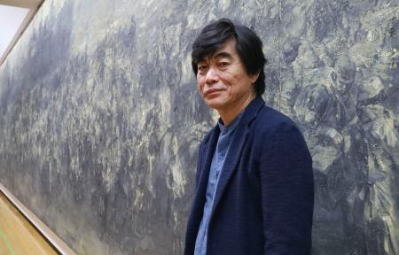 　油絵「一九四六」の前に立つ中国人画家の王希奇さん＝６日午後、福岡市