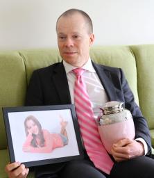 　オーストラリア・メルボルン郊外の自宅で、娘のオリビアさんの遺影と骨つぼを手にするロブ・エバンズさん＝１１月（共同）